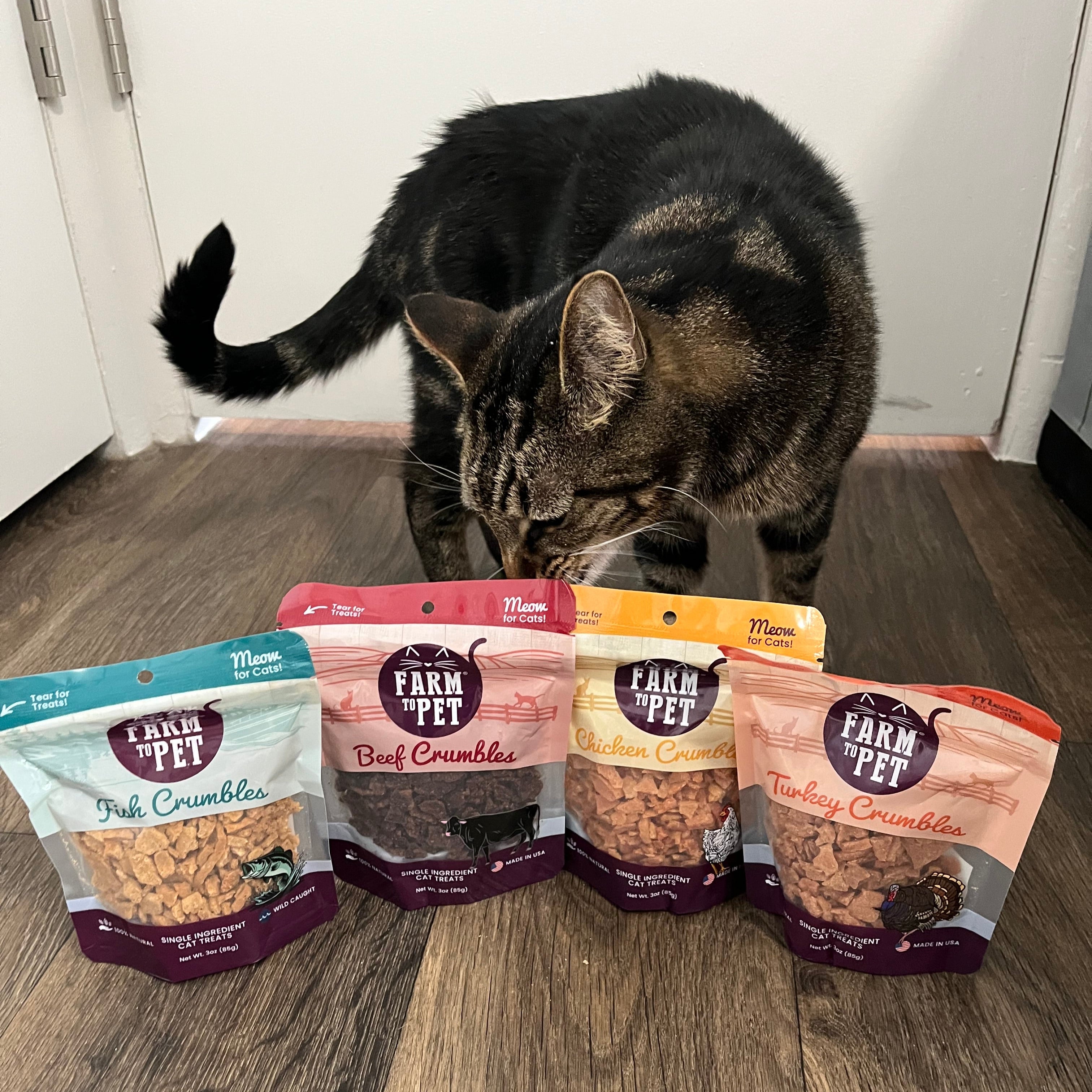 Cat looking at a row of Farm to Pet cat crumble packages on a wooden floor.