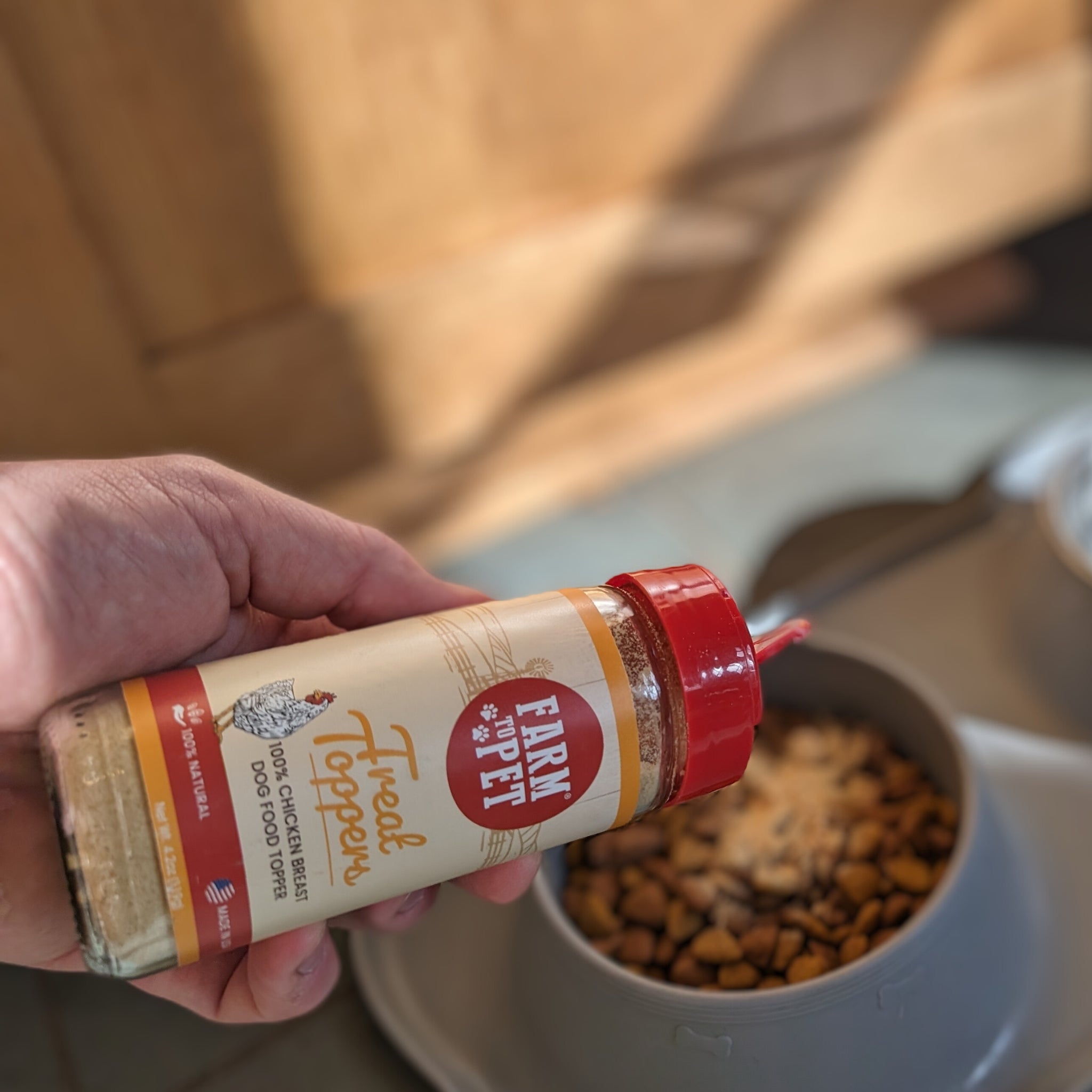 A jar of Farm to Pet Chicken Toppers sprinkled on a bowl of dog food.