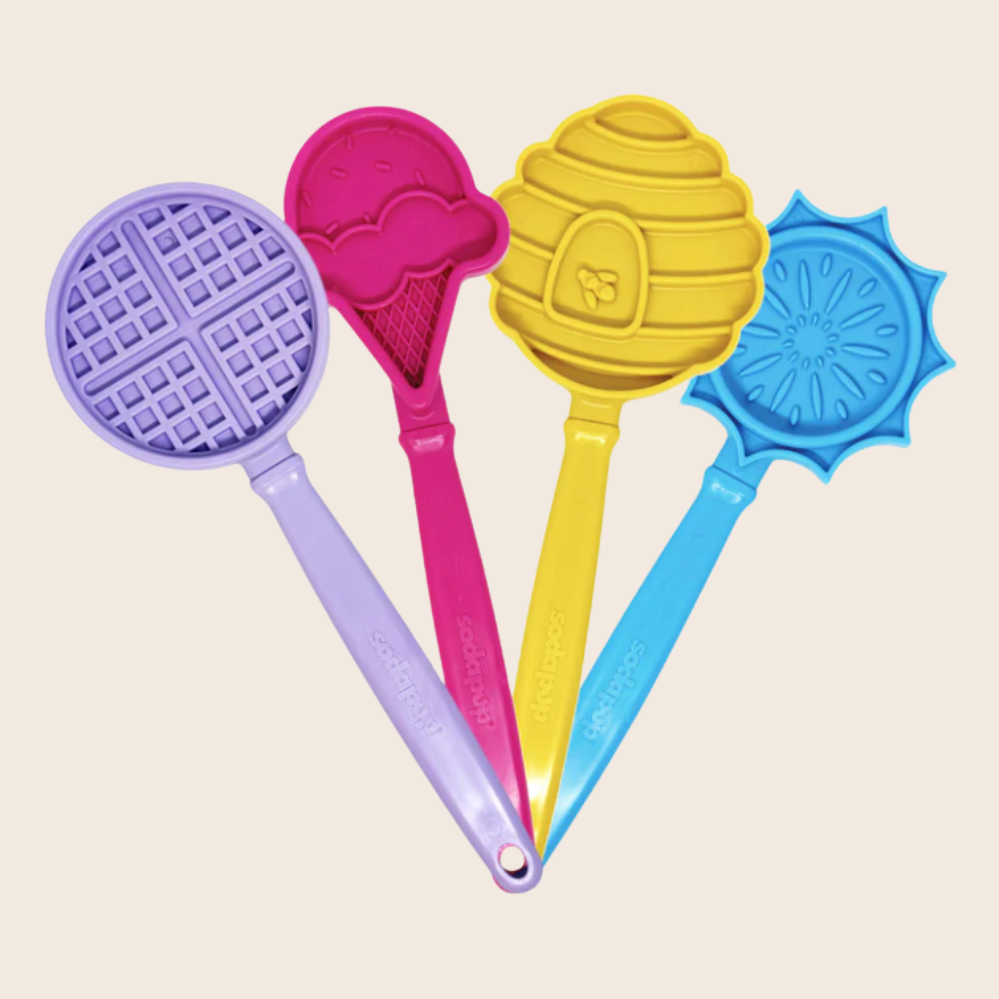 Four colorful lick sticks for dogs with unique shapes on a beige background