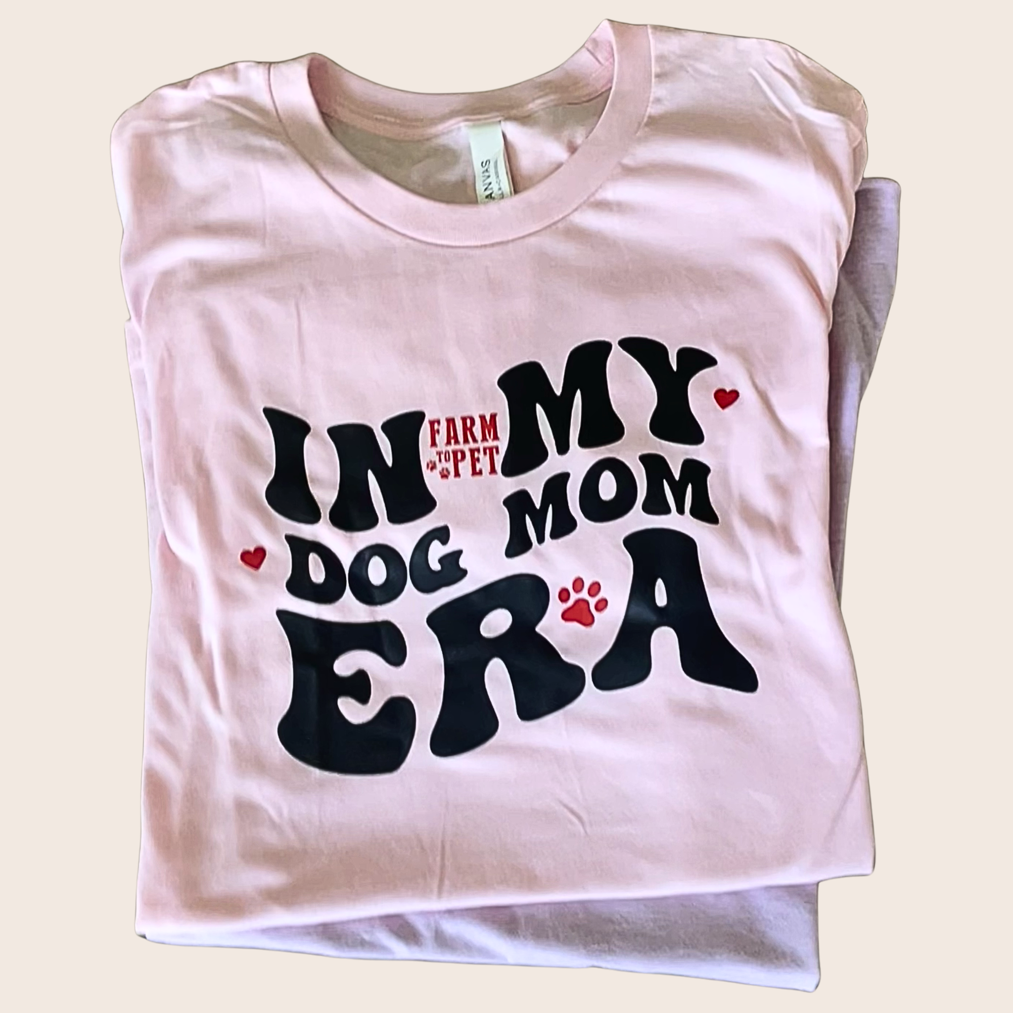 A folded Farm to Pet T-shirt with 'In My Dog Mom Era' text on a beige background.