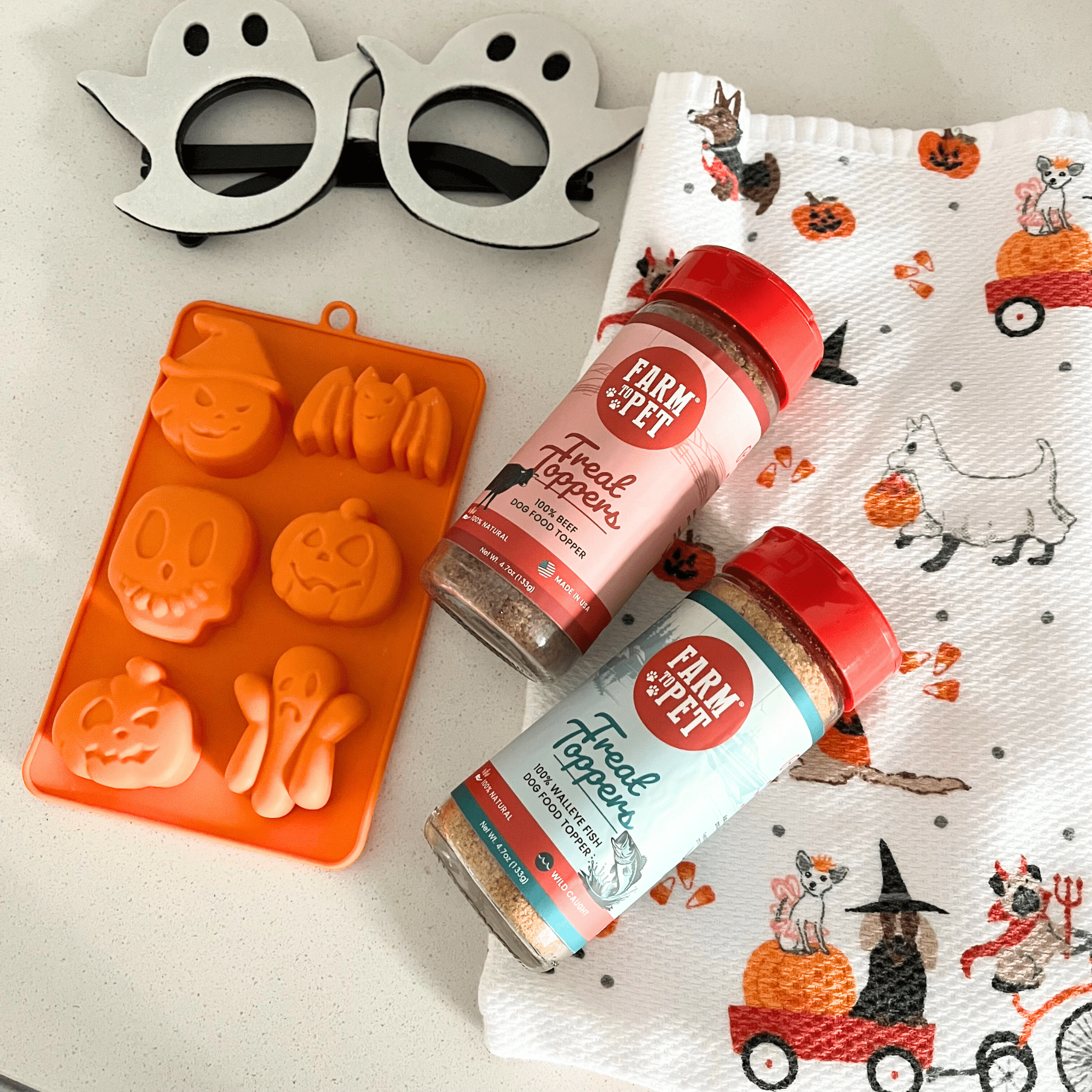 Two bottles of 'Farm to Pet' Treat Toppers with a Halloween-themed mold and napkin in the background.
