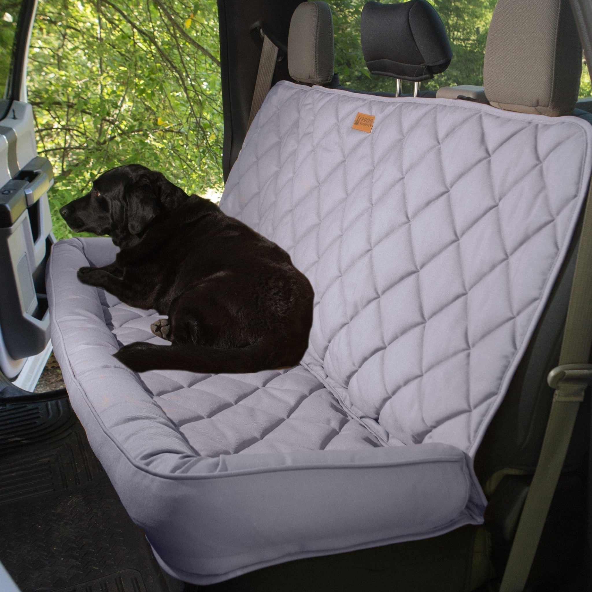 A tan Farm to Pet seat protector for crew cab trucks, fitted in the back seat of a vehicle with a black dog laying on it.