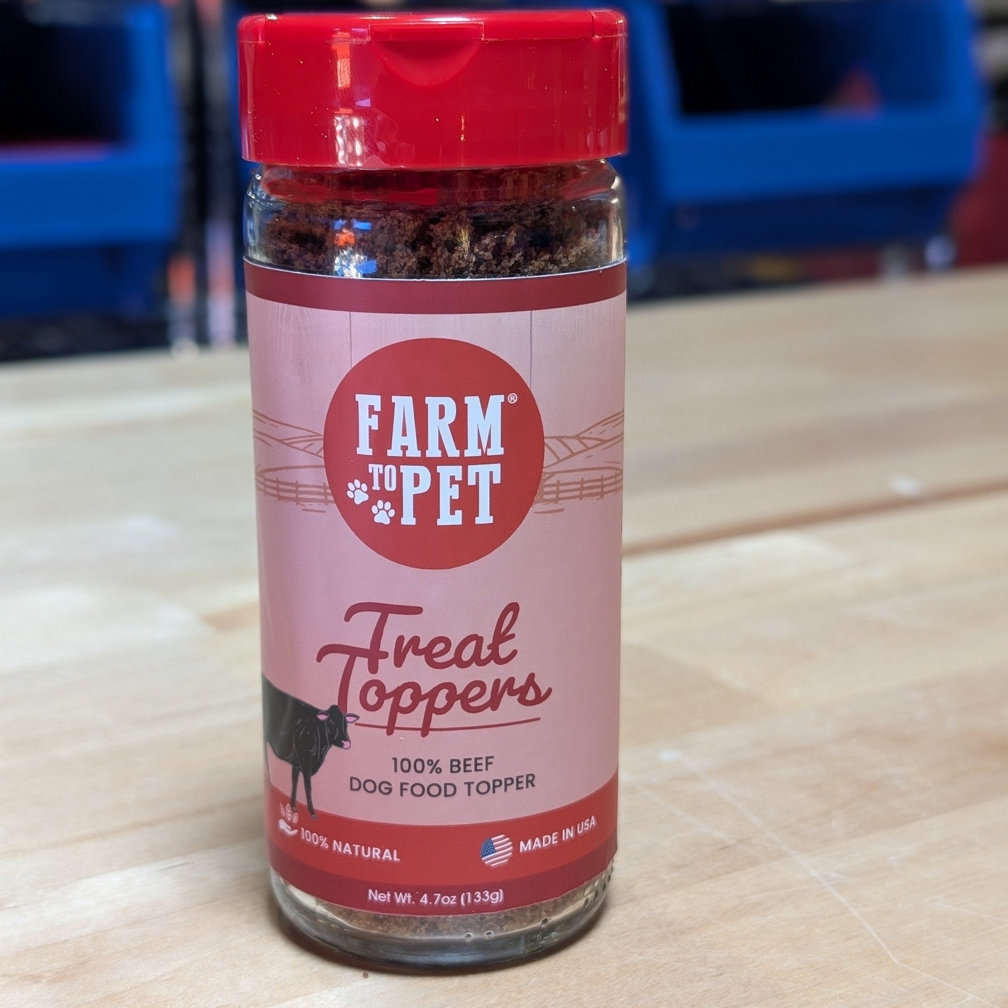 A jar of Farm to Pet Beef Treat Toppers on a wooden surface.