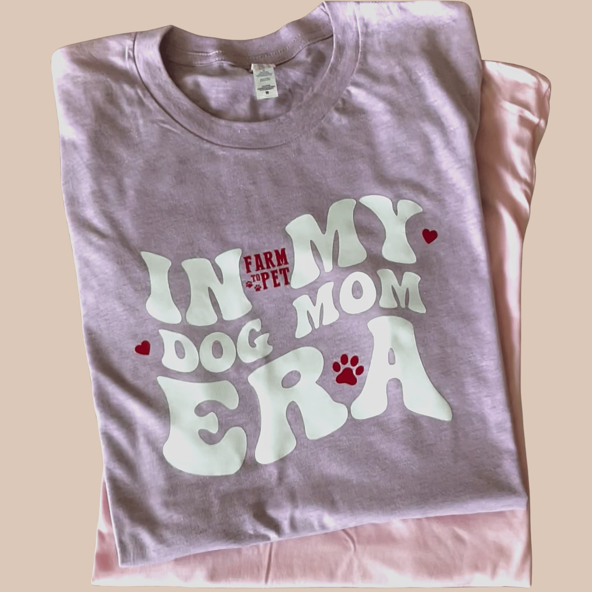 A Farm to Pet purple folded t-shirt with 'In My Dog Mom Era' text on a beige background.