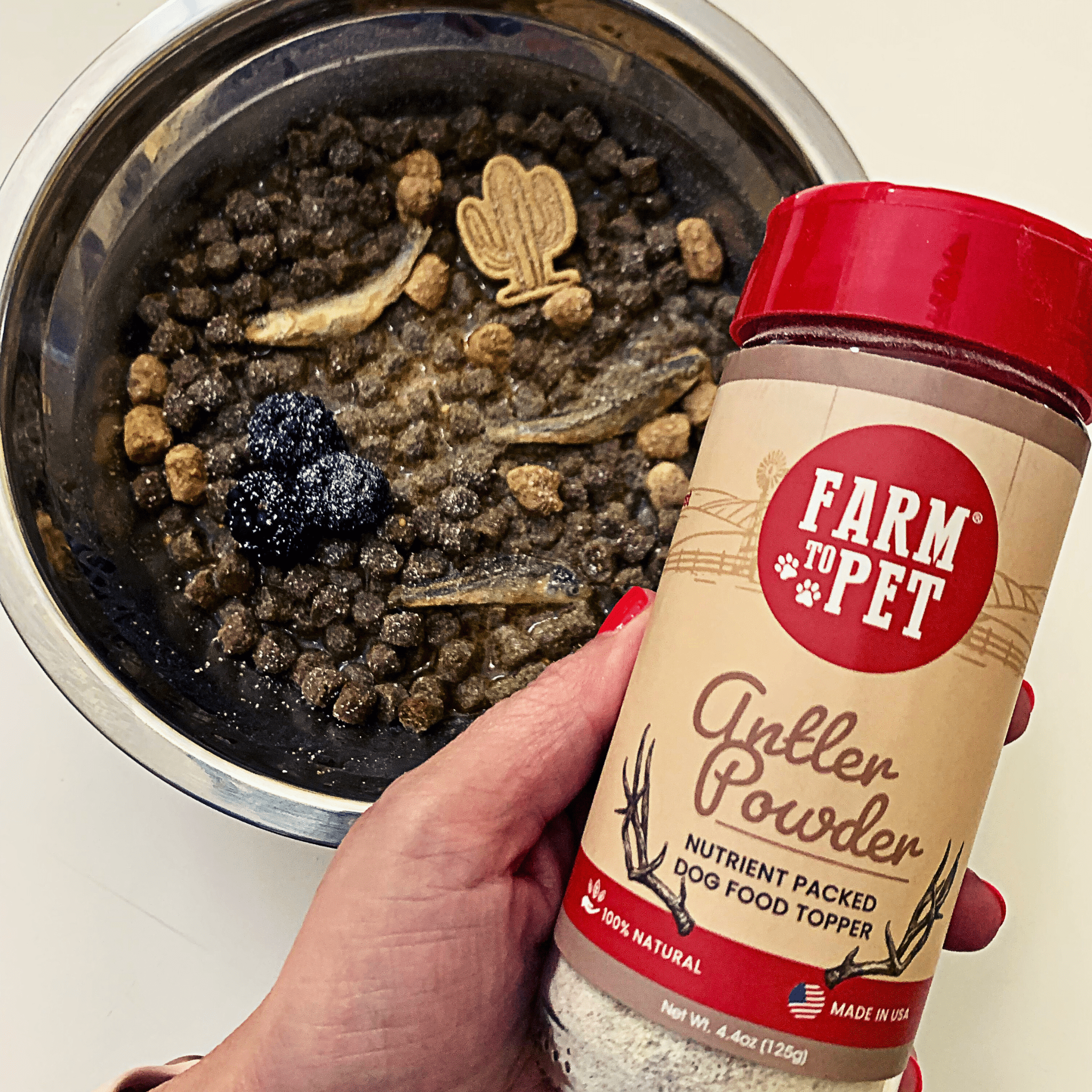 Product of Farm to Pet Elk Antler Powder with a hand holding the bottle and a bowl of dog meal with dried fish, berries, other types of treats and sprinkled with Antler Toppers.