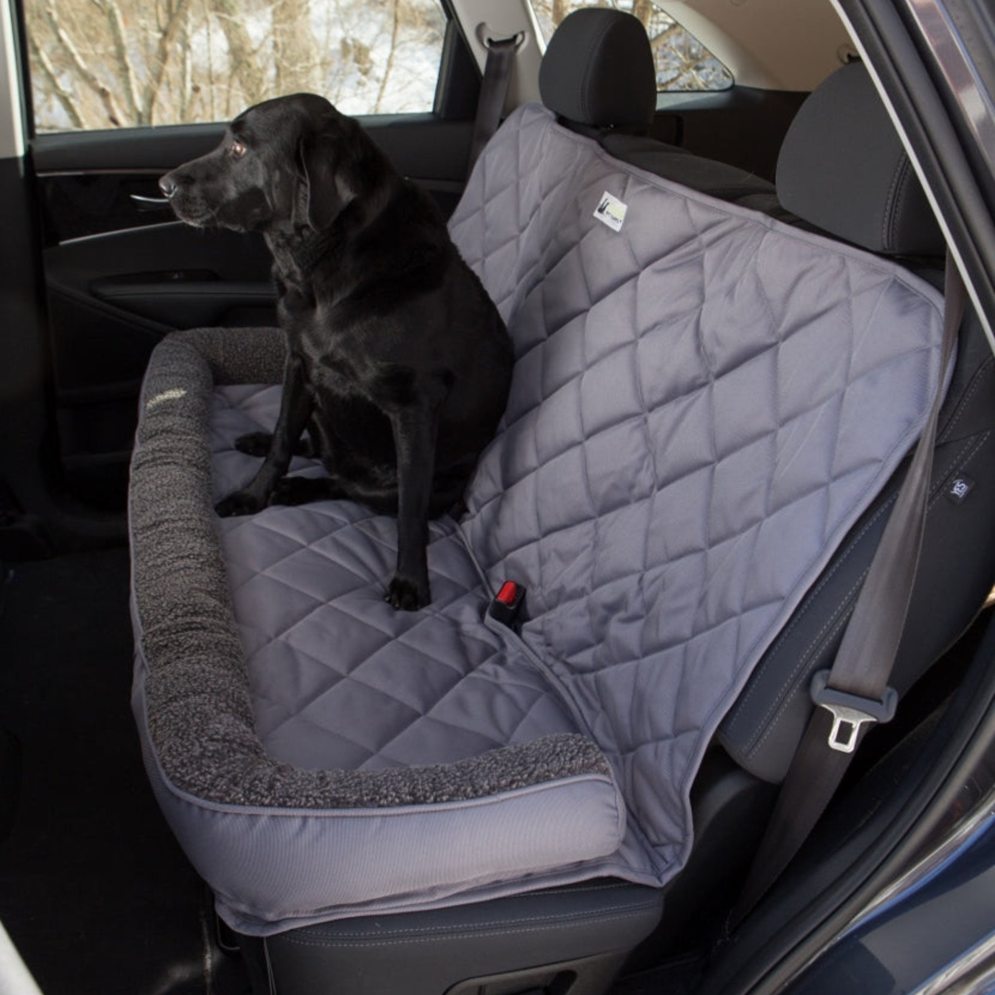 A Farm to Pet gray fleece headrest back seat protector in a car with a black dog sitting on it, showing the protector's fit and the car seat belt opening.