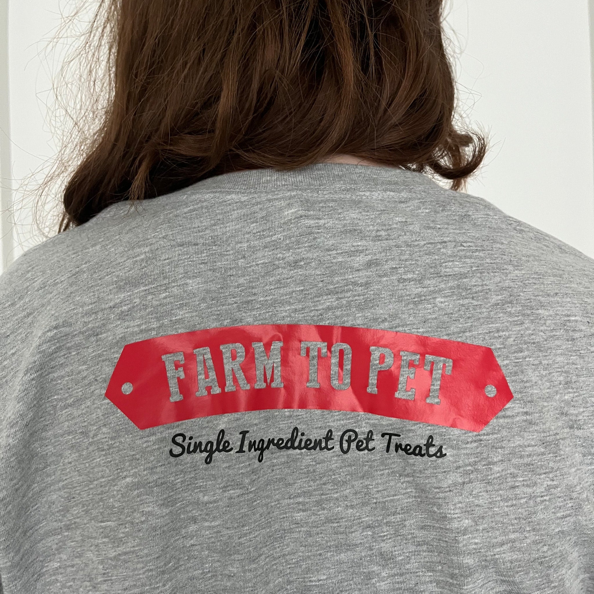 A girl wearing a Gray T-shirt with a red Farm to Pet logo on the back.