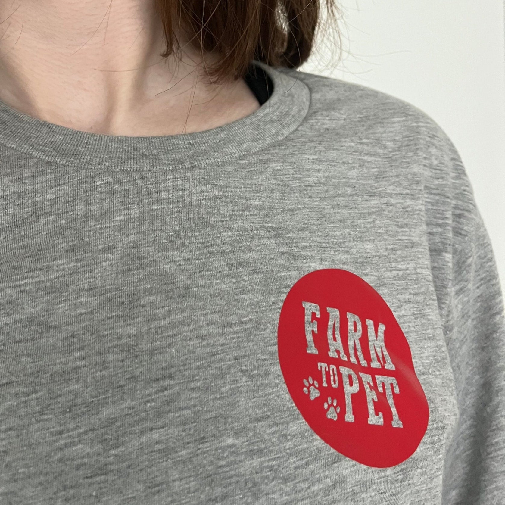 A girl wearing a gray T-shirt with a red 'Farm to Pet' logo on a plain background.