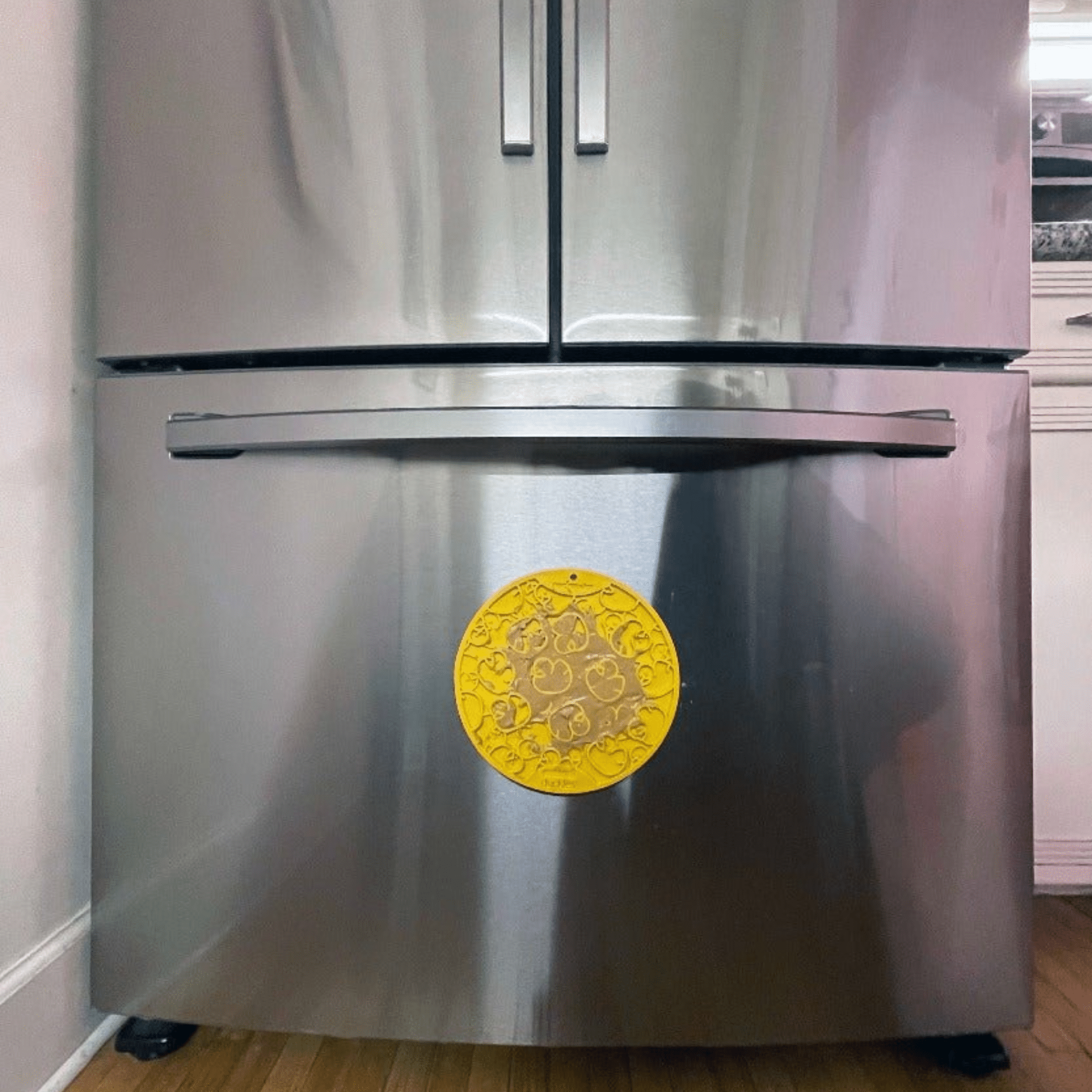Stainless steel refrigerator with a Farm to Pet yellow dog lick mat suctioned to it