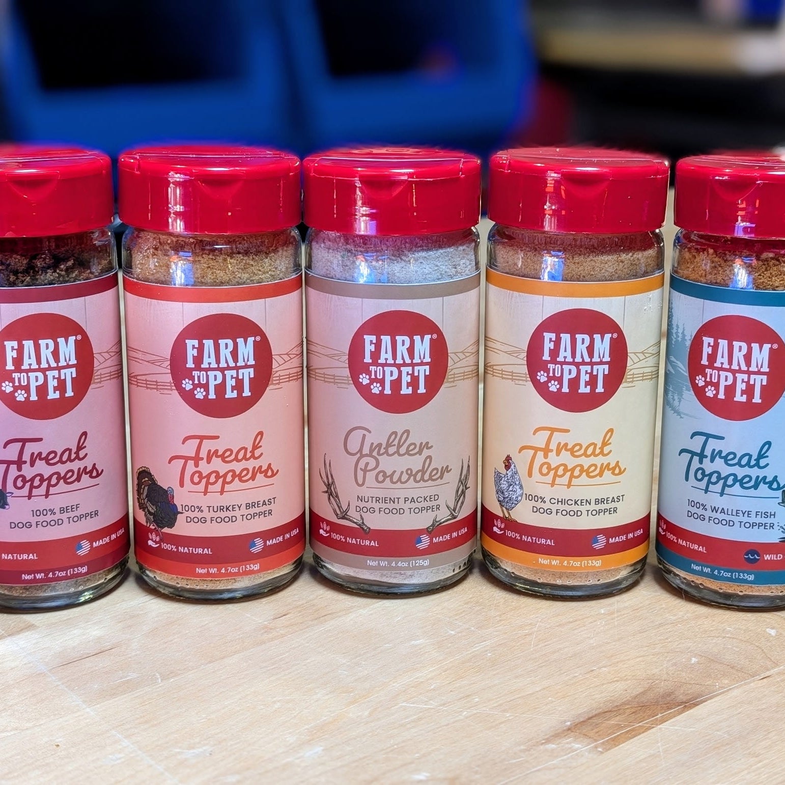 Five bottles of 'Farm to the Pet' Treat Toppers lined up on a wooden surface.