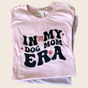 A folded Farm to Pet T-shirt with 'In My Dog Mom Era' text on a beige background.