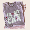 A Farm to Pet purple folded t-shirt with 'In My Dog Mom Era' text on a beige background.