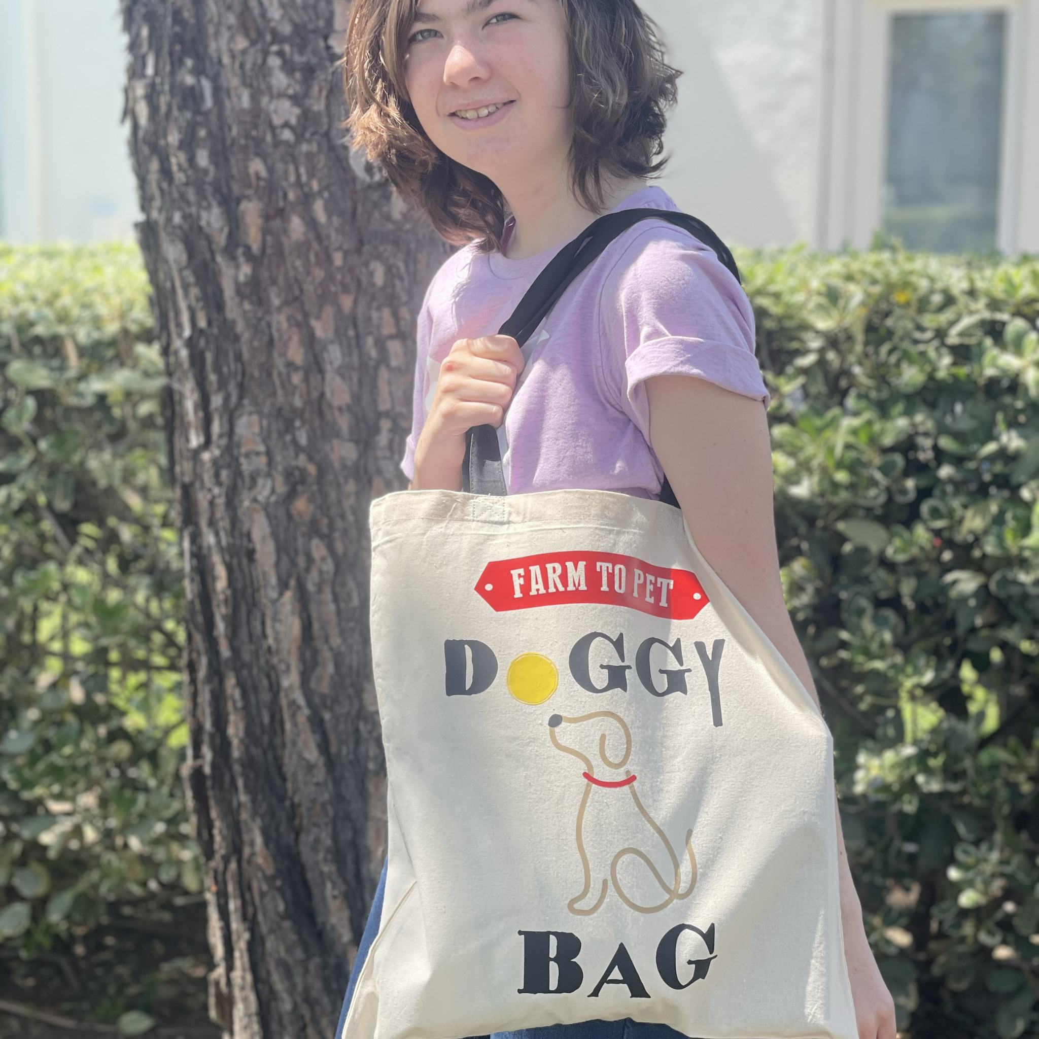 Person holding a tote bag with 'Farm to Pet Doggy Bag' text and graphics outdoors.