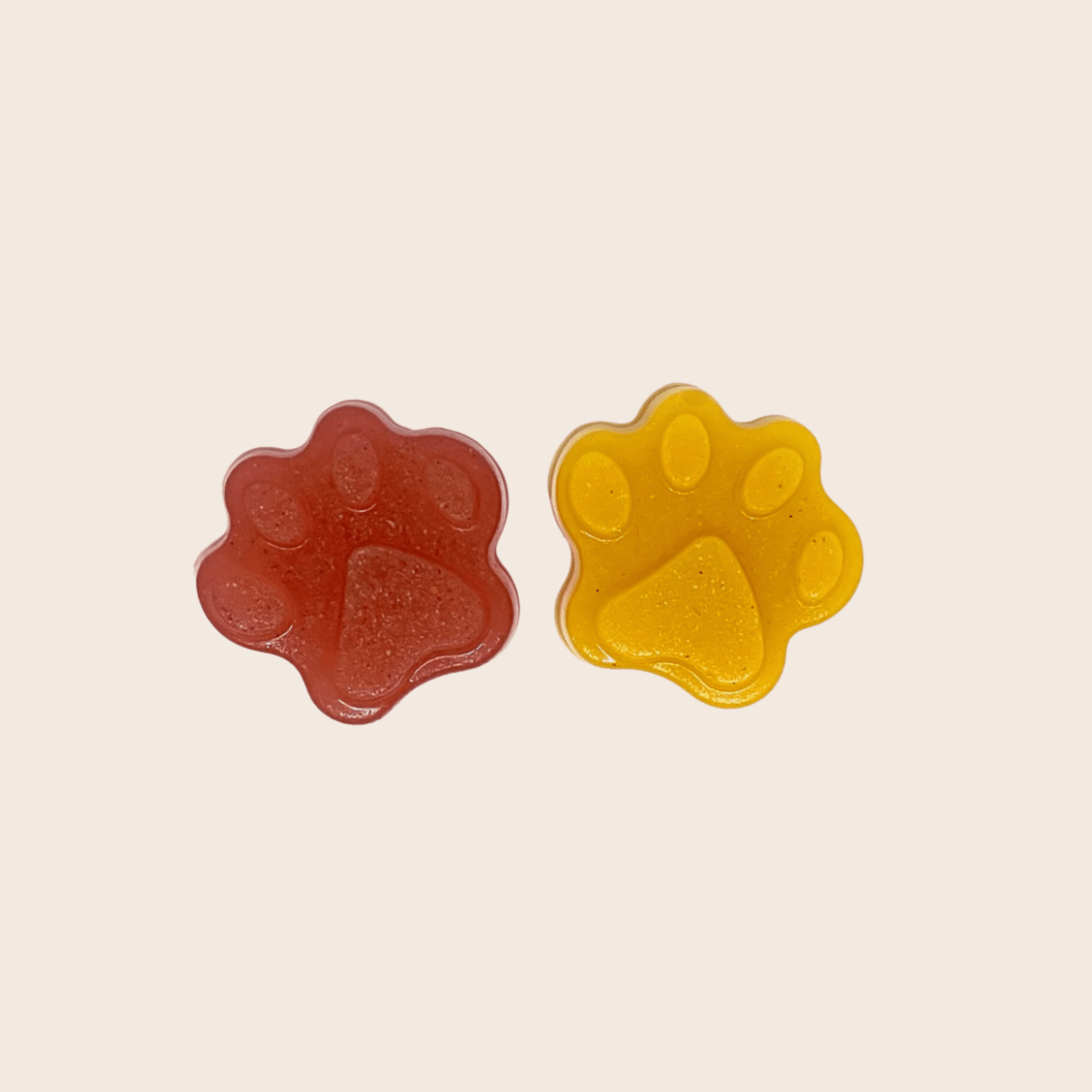 Two gummy bear paw-shaped treats, one red and one yellow, on a beige background.