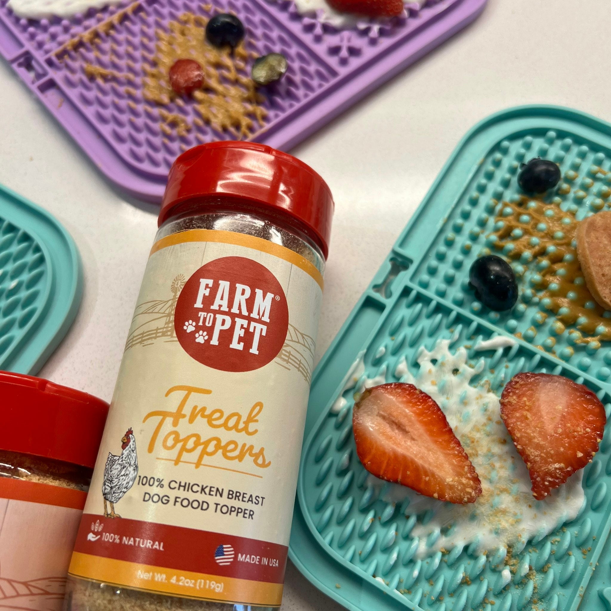 Farm to Pet Chicken Treat Dog Food Toppers on purple and light blue lick mats with strawberries in it sprinkled with our chicken toppers.